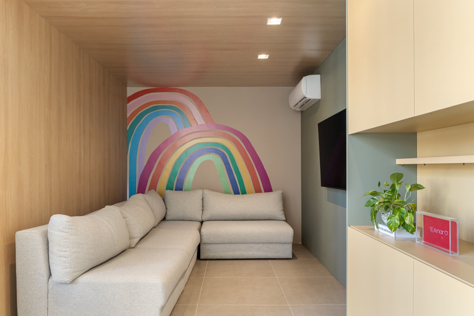 Recepção dos pais com sofá cinza, TV e mural de arco-íris