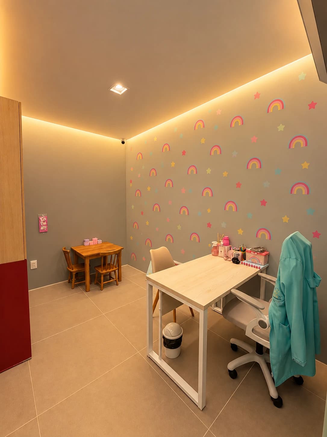 Consultório com parede decorada com arco-íris e estrelas, mesa infantil de madeira e mesa de trabalho