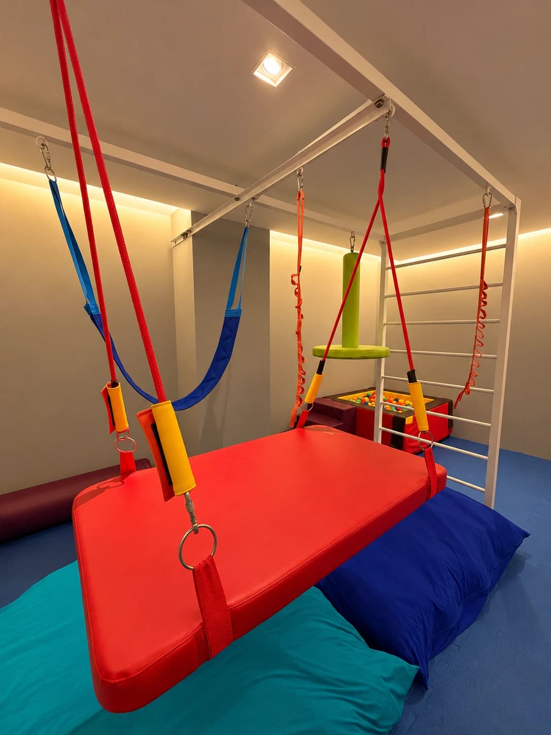 Balanço vermelho suspenso, rede azul e colchões coloridos na sala de terapia ocupacional